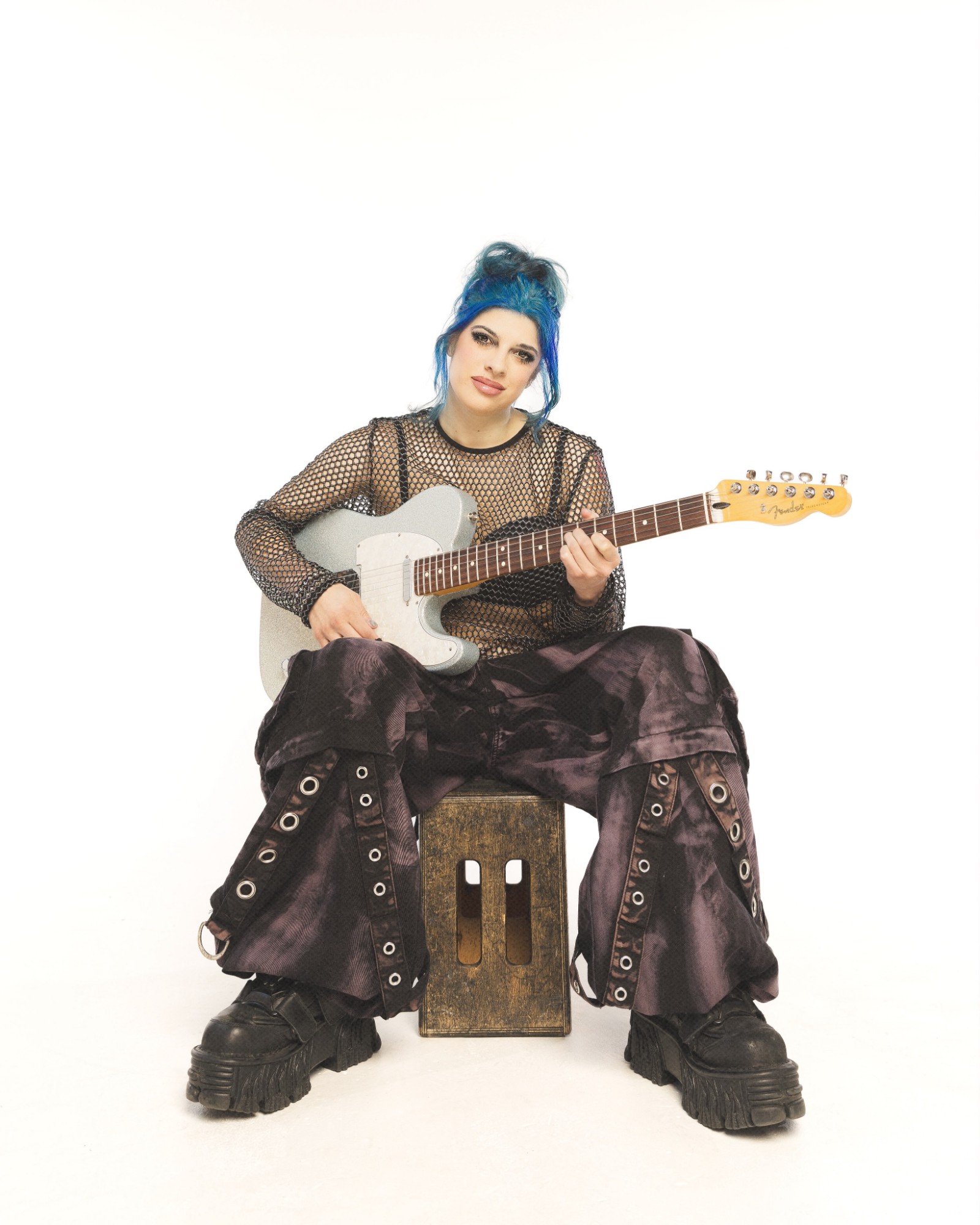 Alex Julia playing an electric guitar, seated on a crate