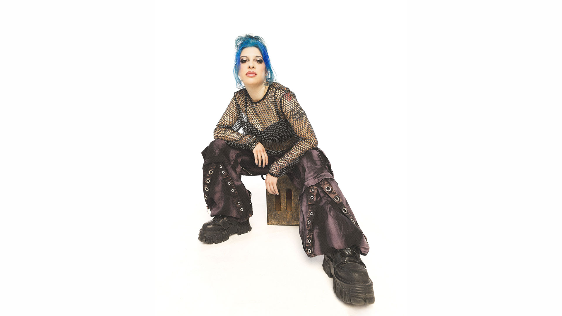 Alex Julia sitting on a wooden crate in a white studio
