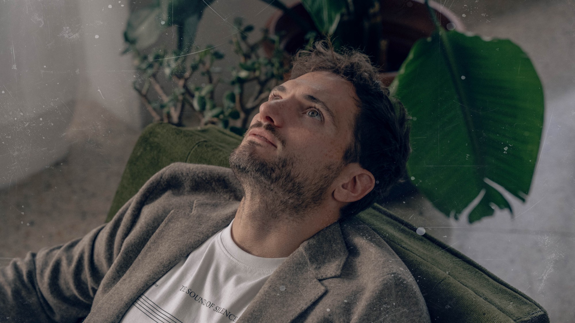Alfredo Salvati of colourshop leaning back in a green armchair, looking up, with plants behind him