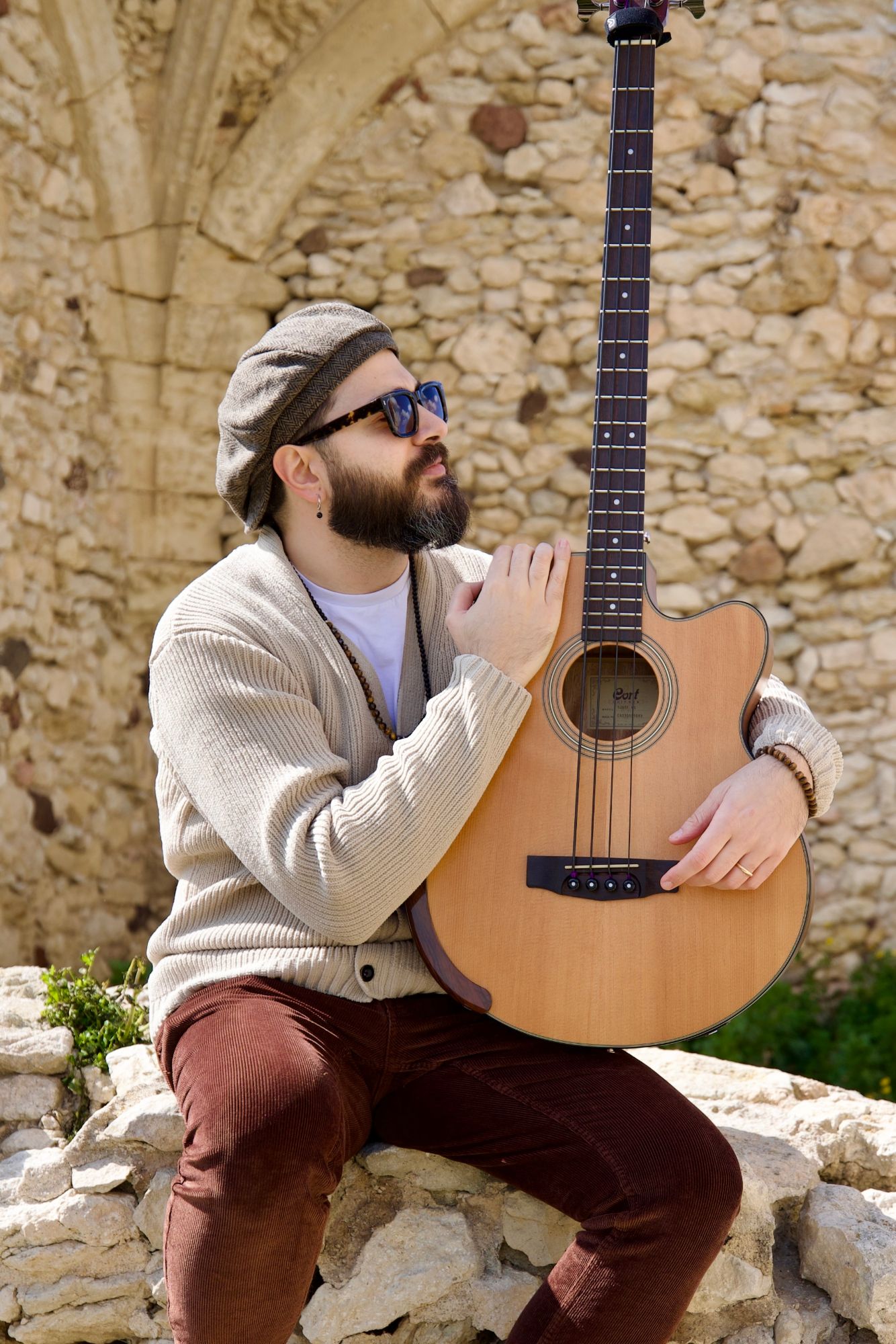 Pier Piras sitting on a stone wall with his acoustic bass guitar